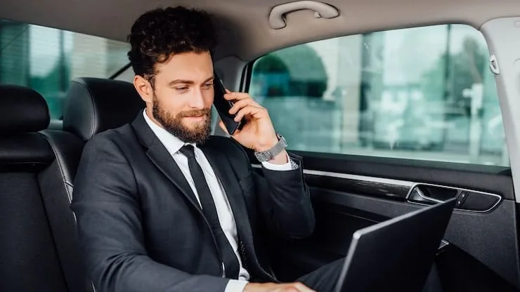 Executivo de terno no banco traseiro, ao telefone e com o notebook aberto